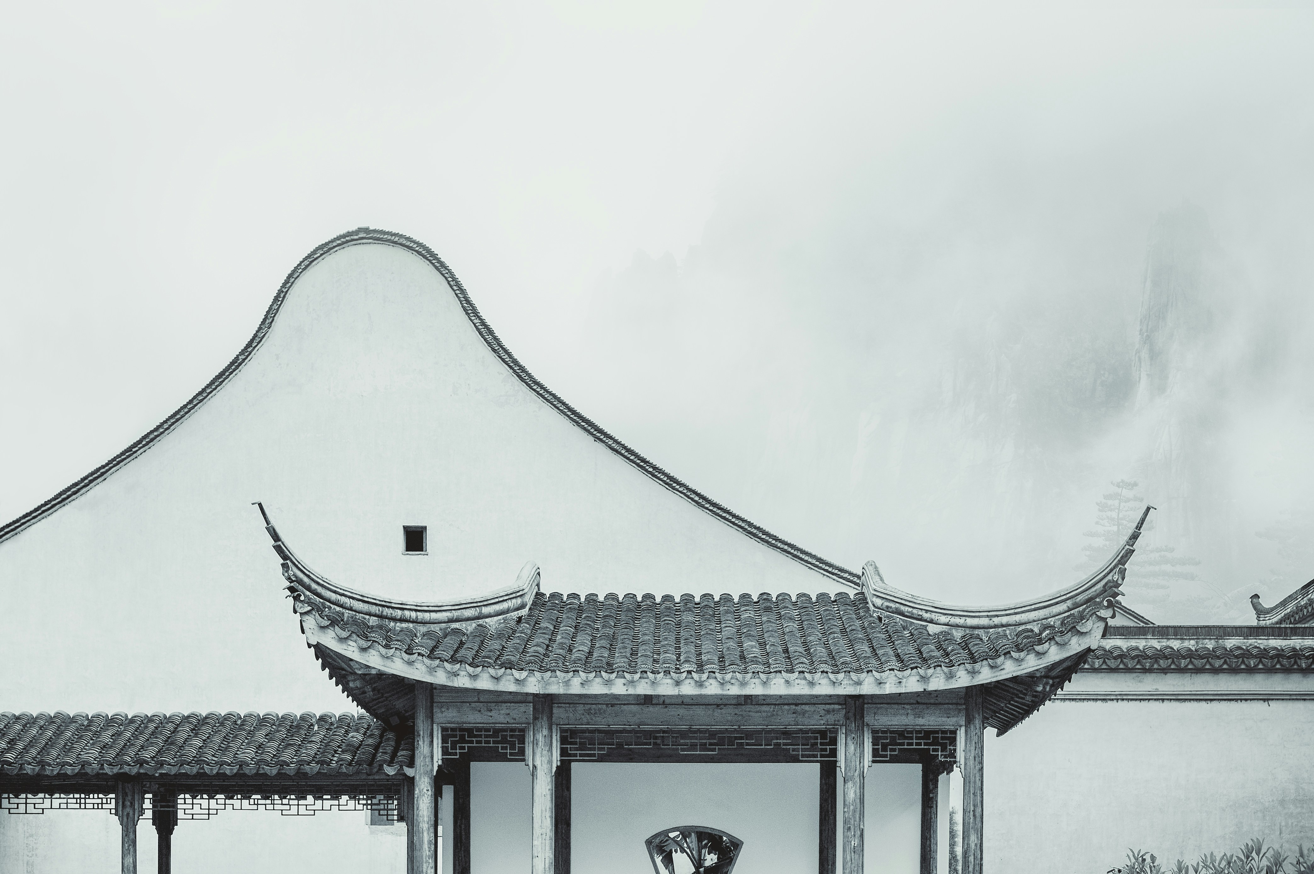 Une photo sereine en noir et blanc d'un pavillon chinois traditionnel avec un toit courbé, sur fond de montagnes brumeuses, évoquant un sentiment de sagesse ancienne.