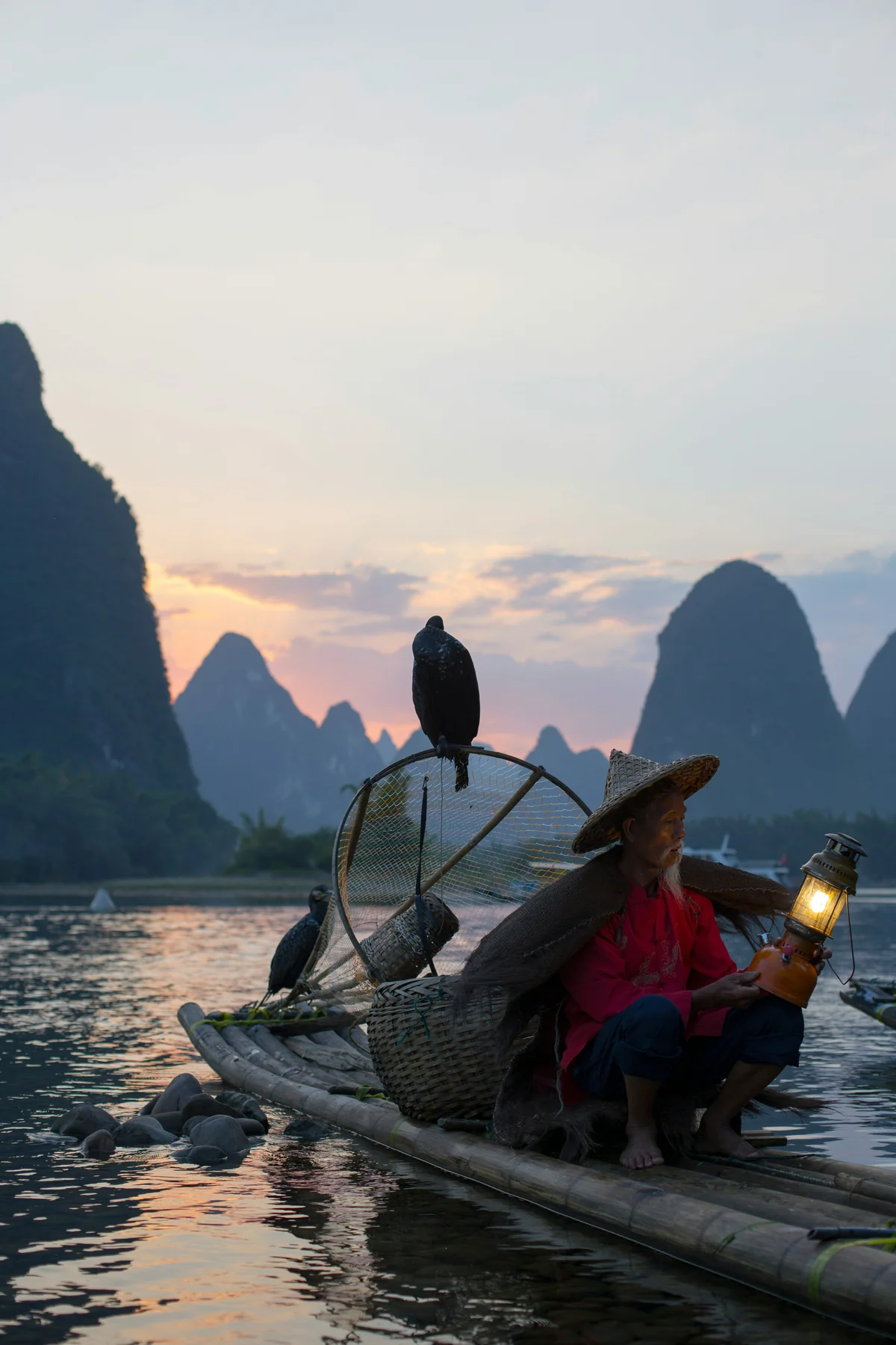 A wise, elderly fisherman with cormorant birds on his bamboo raft at dusk, symbolizing experience, patience, and a deep connection to nature rhythms.