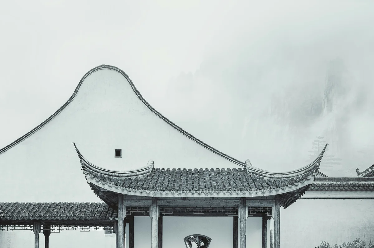 A serene black and white photo of a traditional Chinese pavilion with a curved roof, set against a misty mountain backdrop, evoking a sense of ancient wisdom.